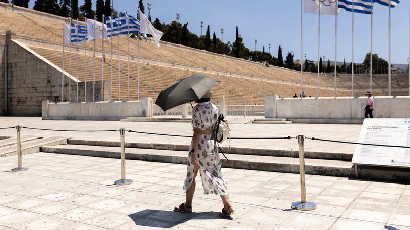 Eine Touristin mit einem Schirm geht vor dem Panathinaiko-Stadion entlang