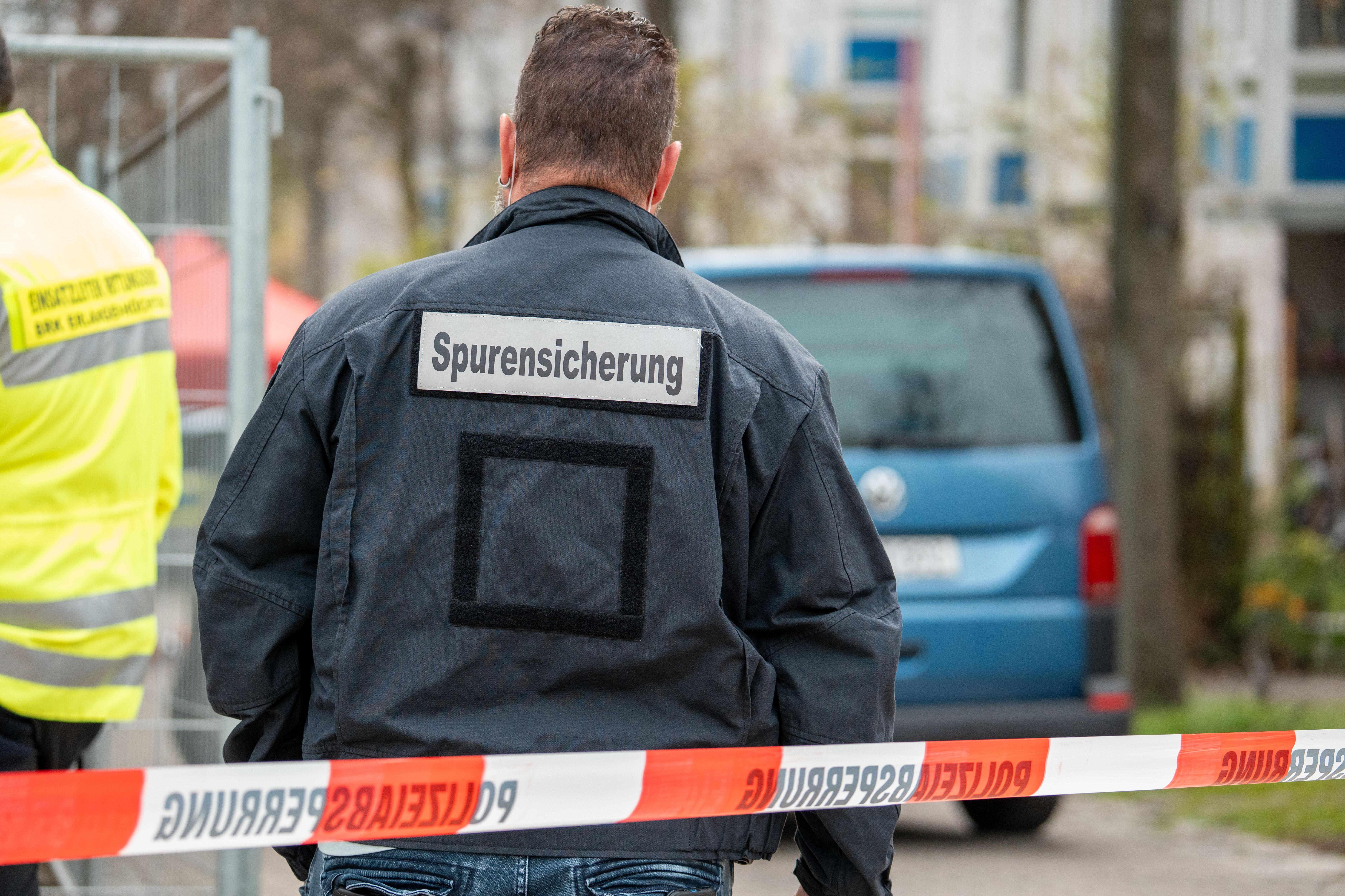 Ein Mann mit der Aufschrift "Spurensicherung" steht hinter einer Polizeiabsperrung.