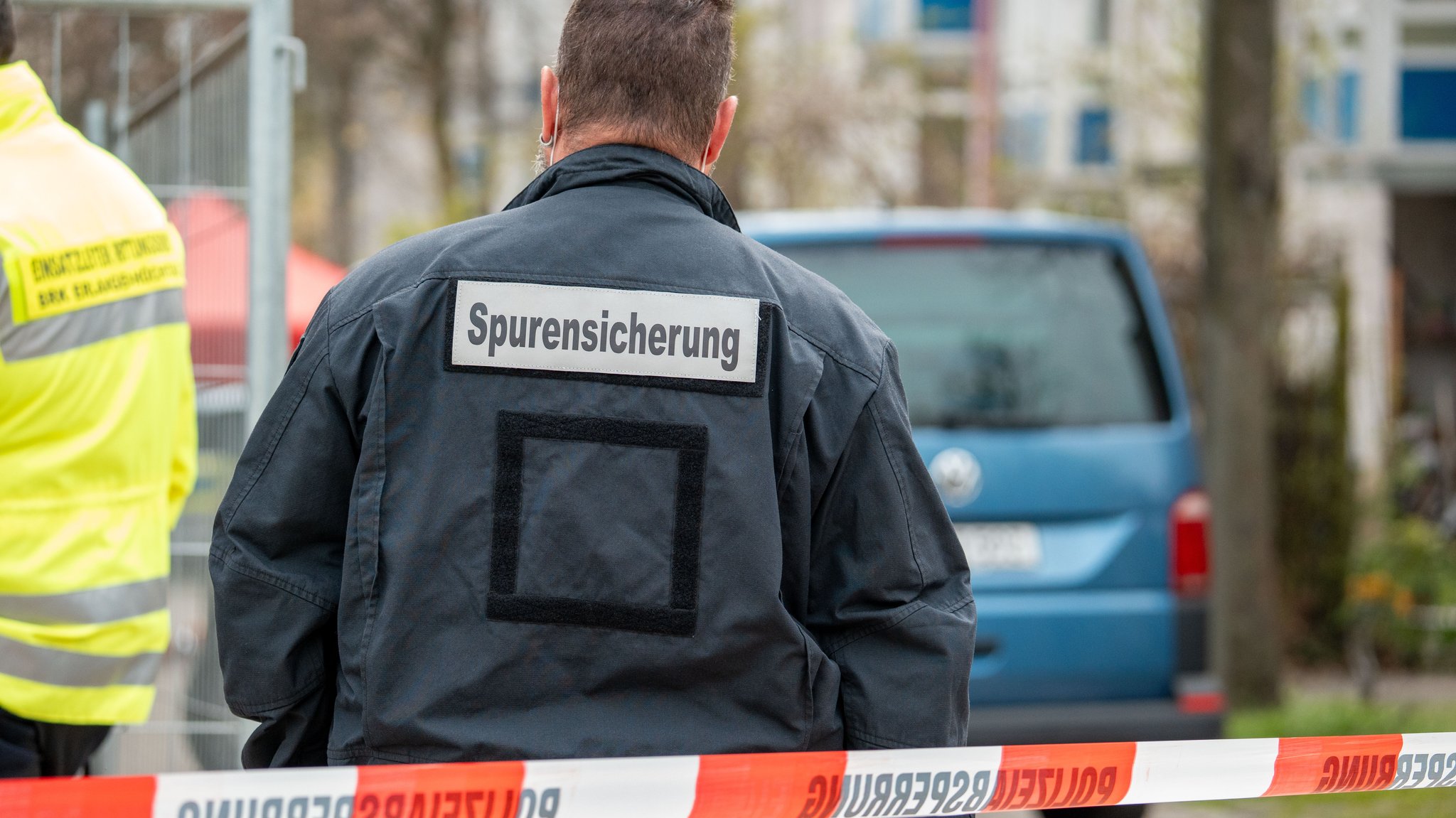 Ein Mann mit der Aufschrift "Spurensicherung" steht hinter einer Polizeiabsperrung.