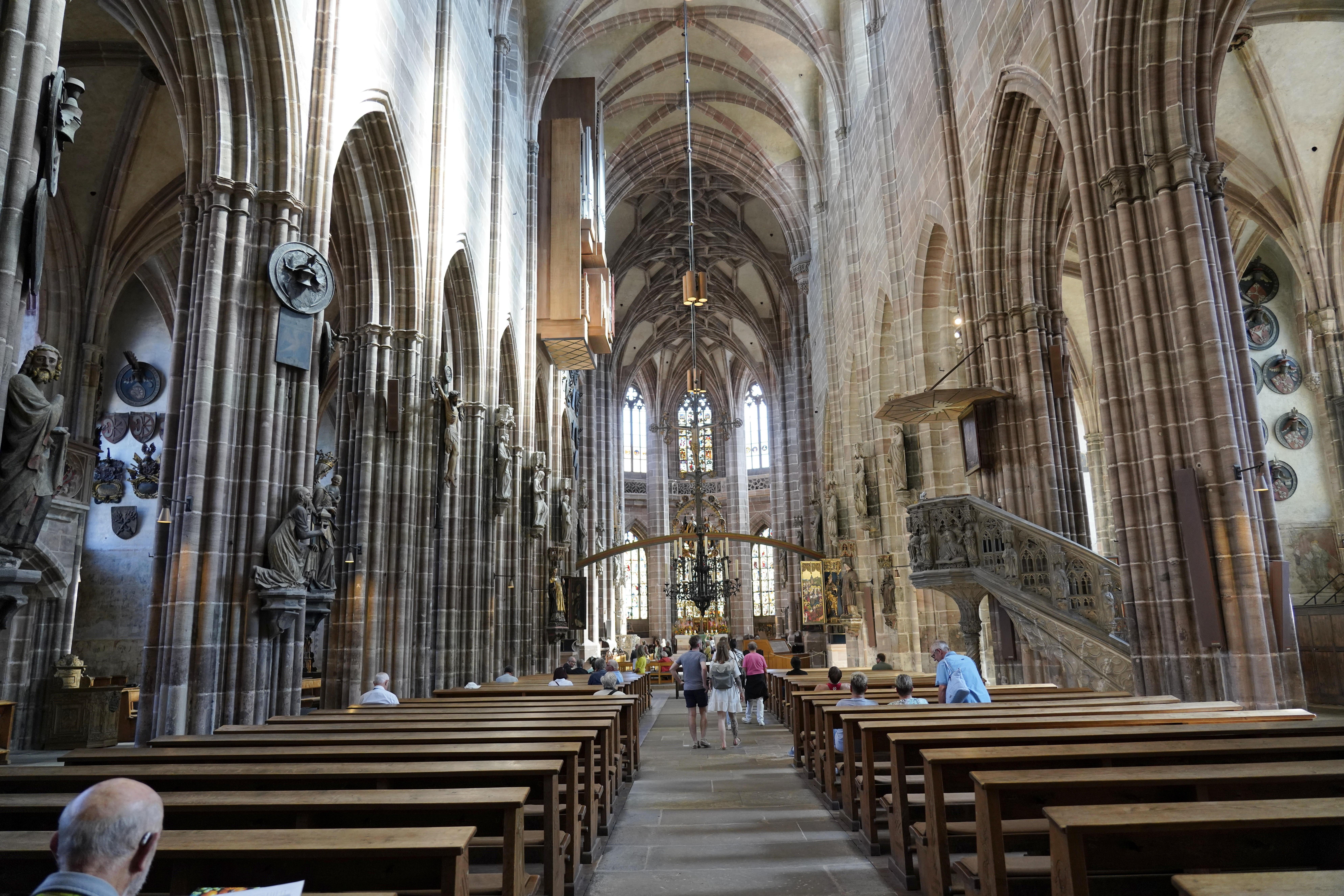 Kirchenschiff mit hohen Gewölben, Bänken und Menschen im Inneren der historischen Kirche St. Lorenz in Nürnberg.