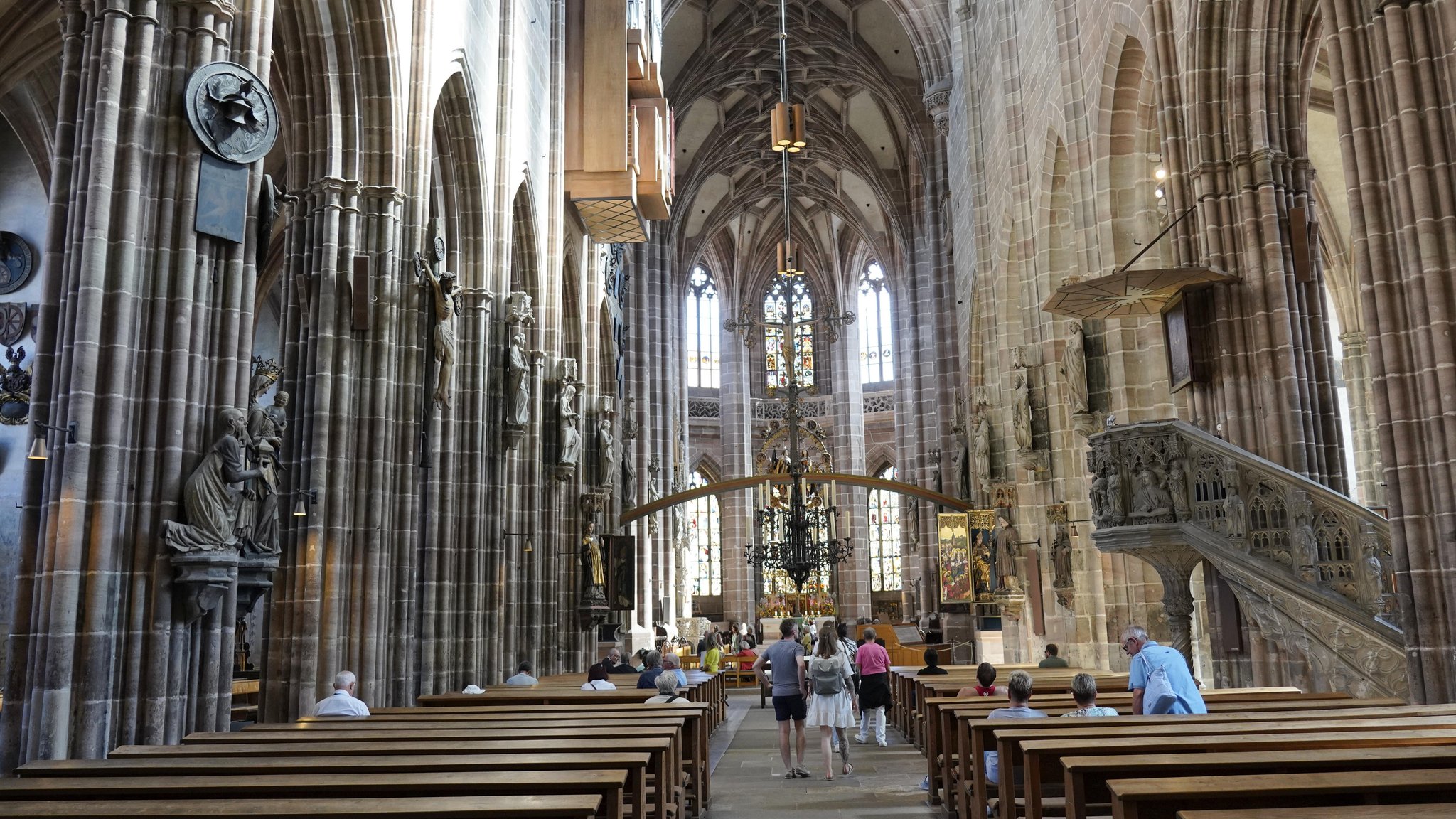 Kirchenschiff mit hohen Gewölben, Bänken und Menschen im Inneren der historischen Kirche St. Lorenz in Nürnberg.