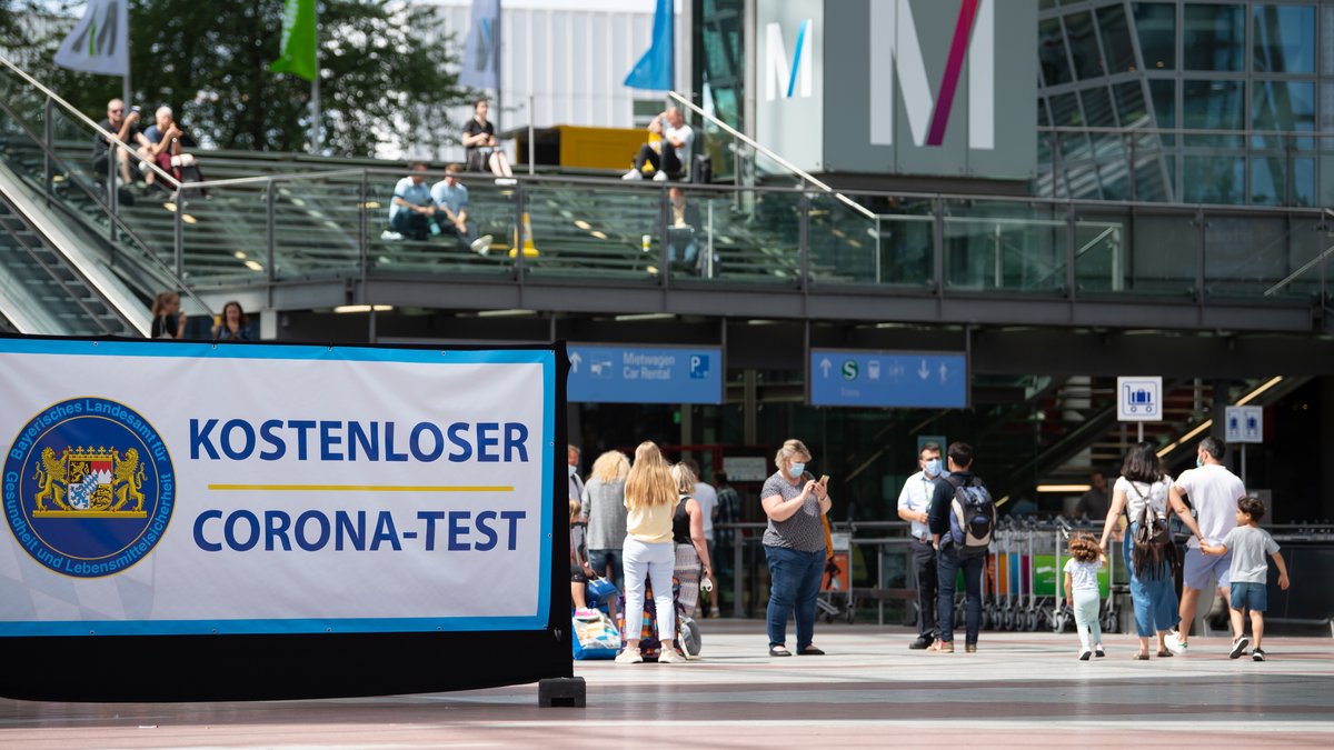 Flugreisende gehen am Flughafen München an einem Schild mit der Aufschrift "Kostenloser Corona-Test" entlang.