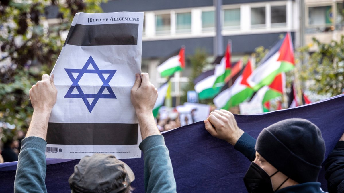 Symbolbild: Ein Pro-Israelischer Gegendemonstrant zeigt eine jüdische Zeitung mit einem Davidstern, im Hintergrund Pro-Palästinensische Demonstranten.