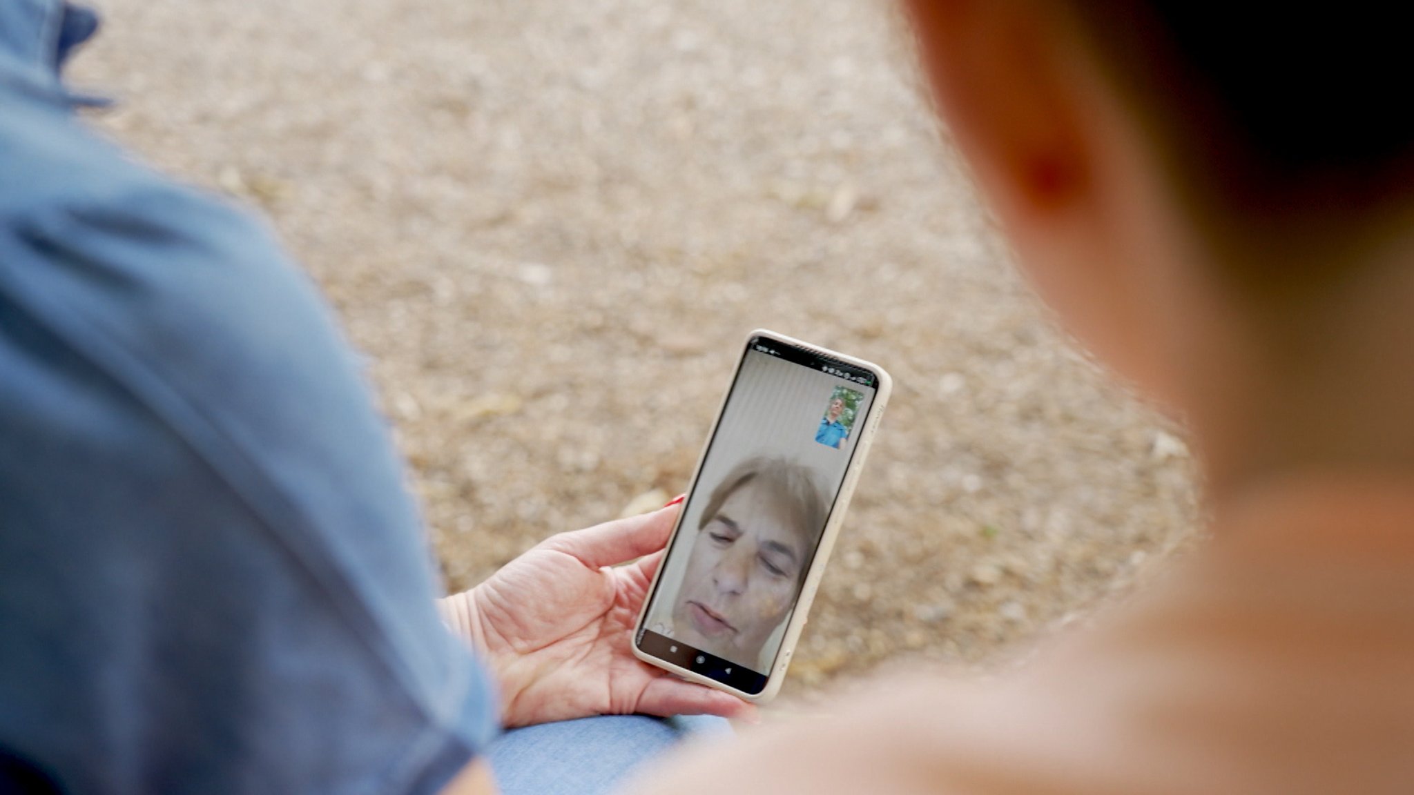 Eine Frau hält ein Handy auf dem ein Videoanruf mit ihrer Mutter zu sehen ist.