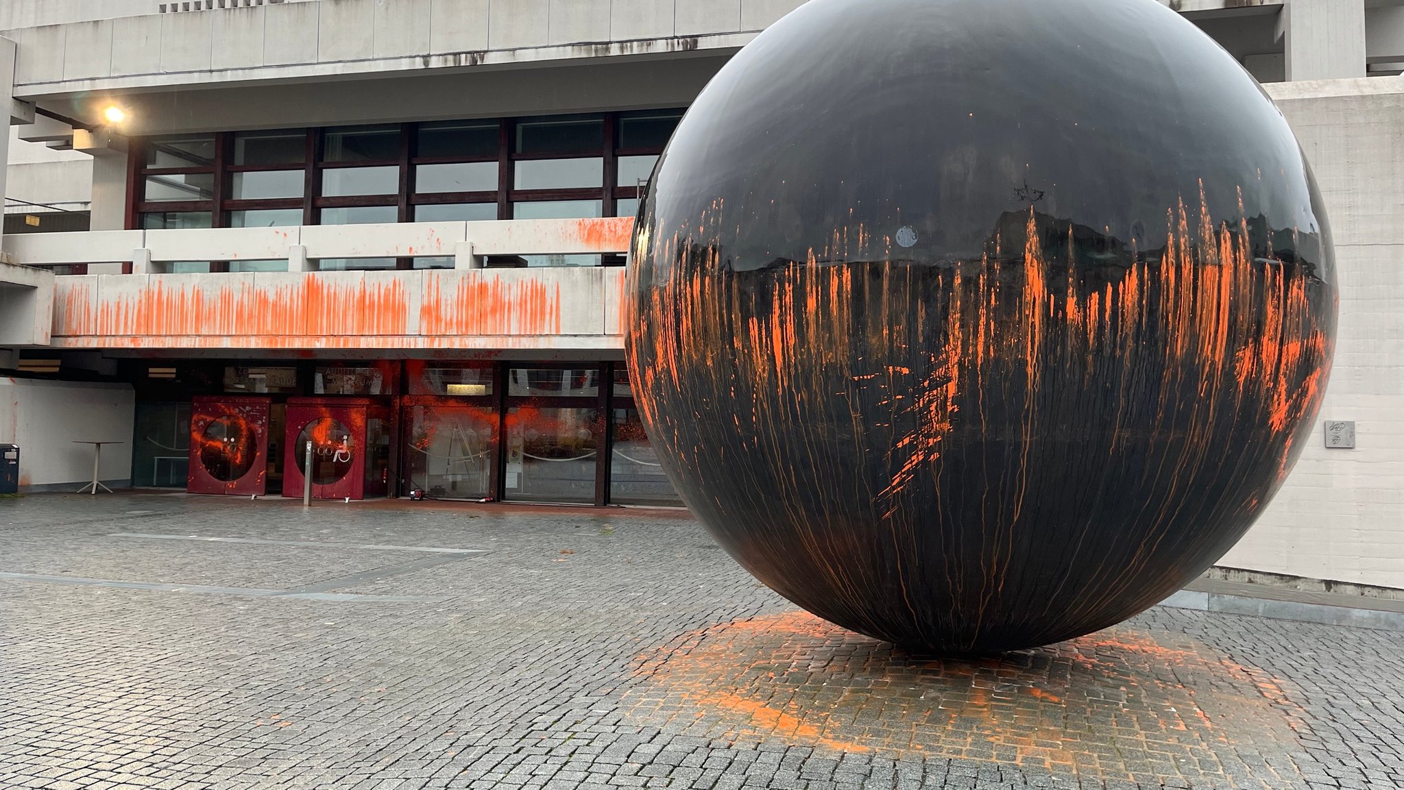 Campus der Universität Regensburg, Fassade und eine große Metallkugel davor sind mit oranger Farbe besprüht