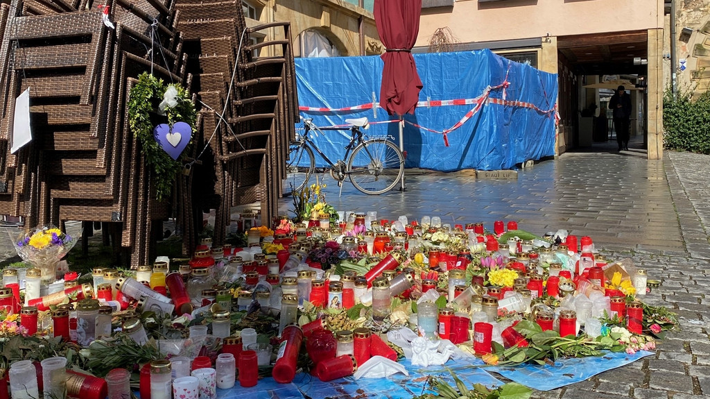 Blumen und Kerzen stehen auf dem Boden vor dem Tatort.