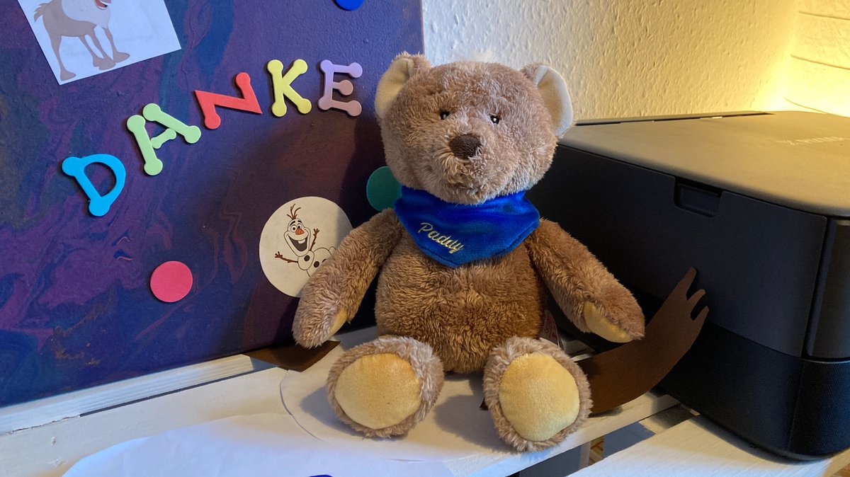 Der Teddybär hat extra lange Arme und Beine. Auf seinem Halstuch steht "Päddy".