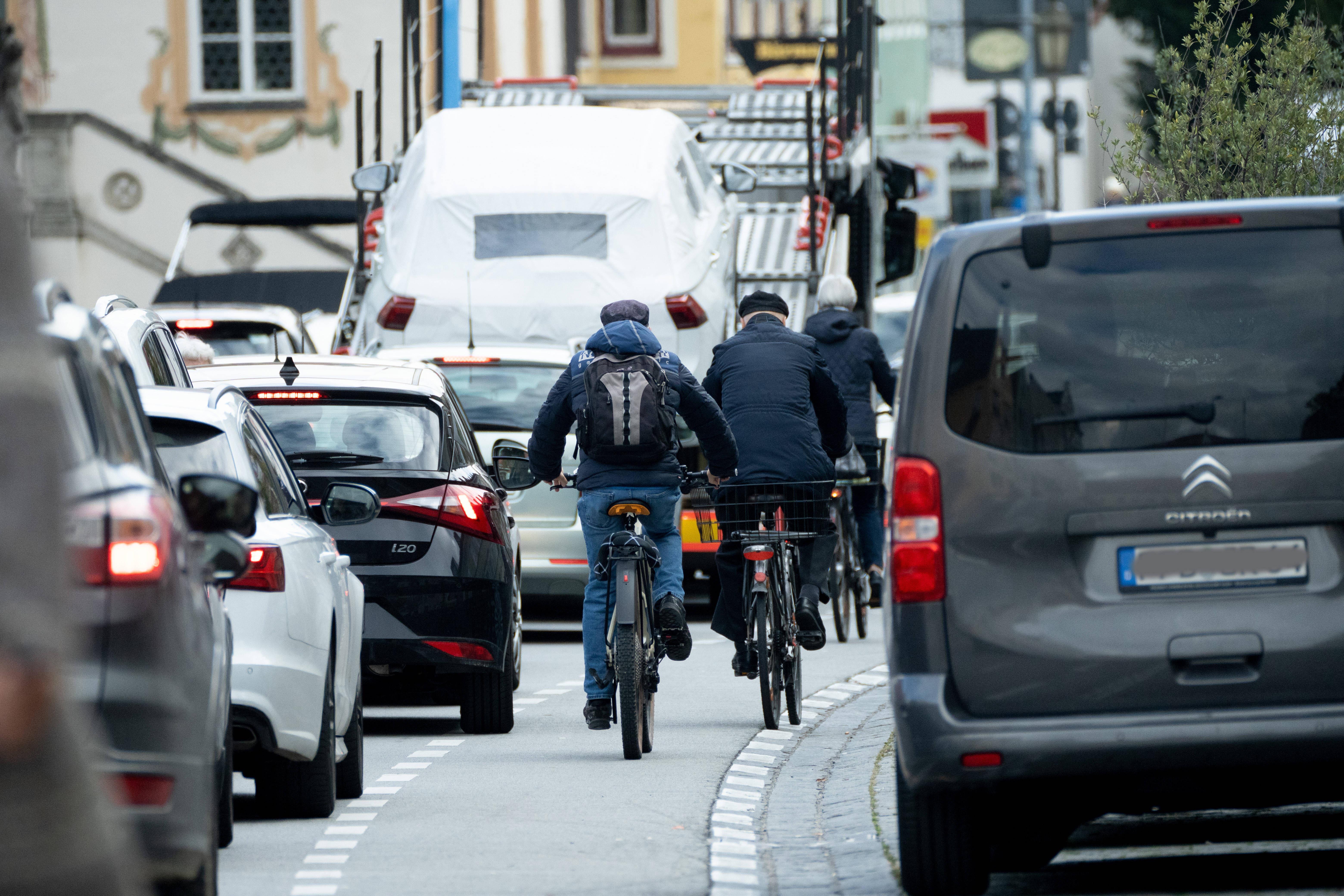 Autos stauen sich in der Stadt, dazwischen radeln Fahrradfahrer auf einer engen Fahrradspur.