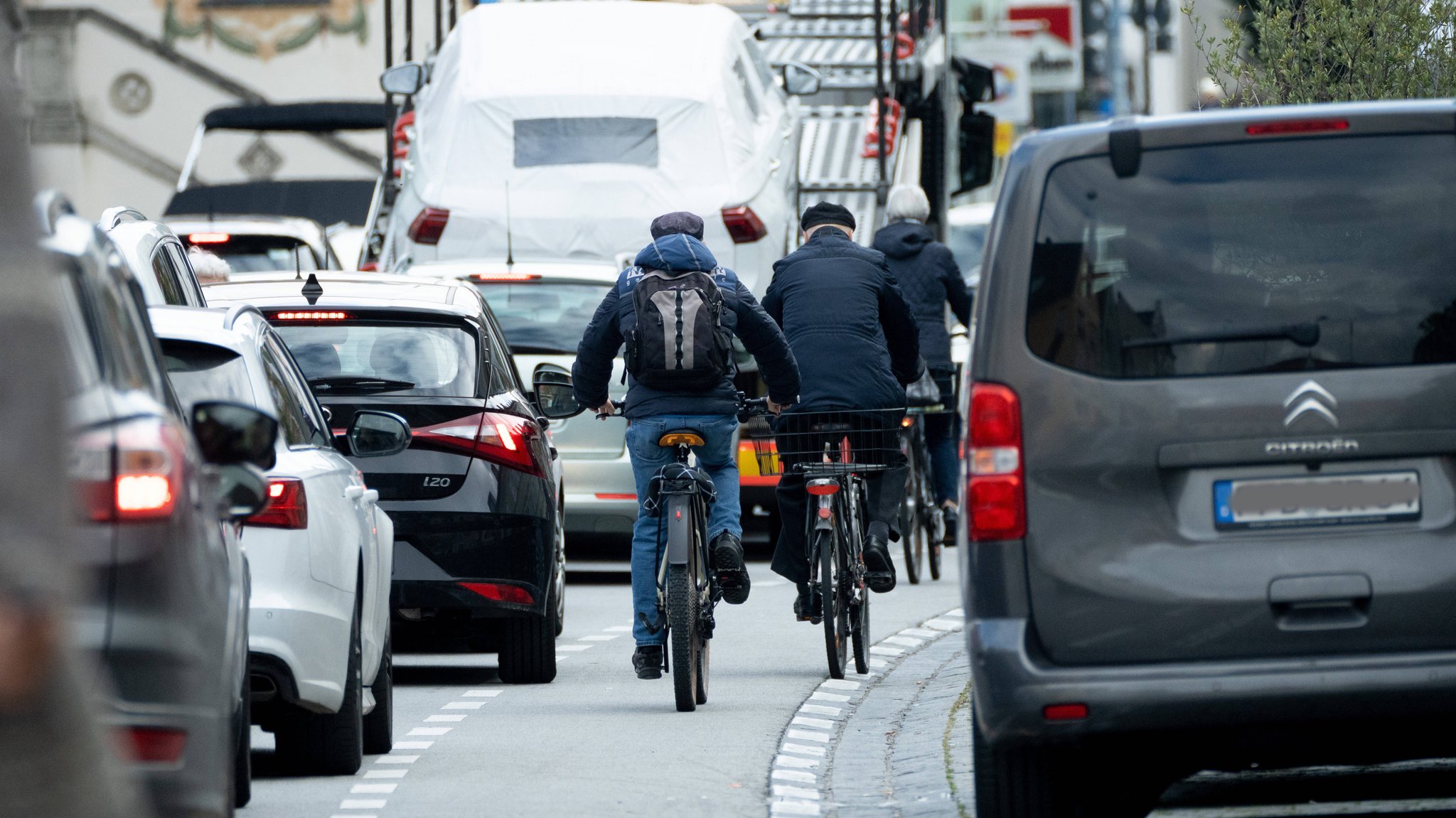 Autos stauen sich in der Stadt, dazwischen radeln Fahrradfahrer auf einer engen Fahrradspur.