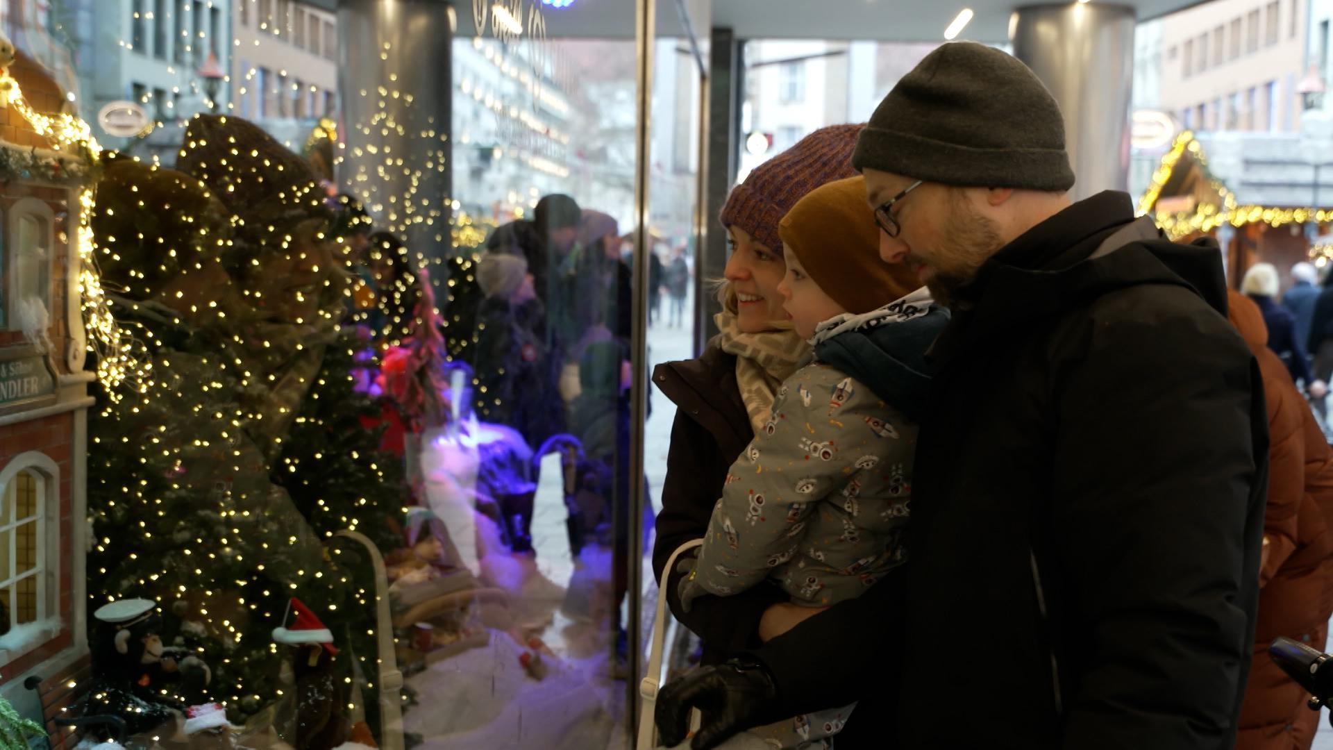 Eine Familie betrachtet ein festlich geschmücktes Schaufenster von außen.