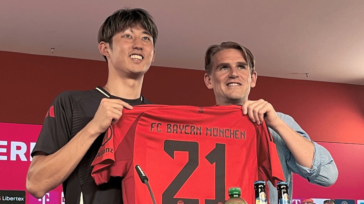 Hiroki Ito (l), Neuzugang des FC Bayern München, und Münchens Sportdirektor Christoph Freund halten während seiner Präsentation Itos neues Trikot.