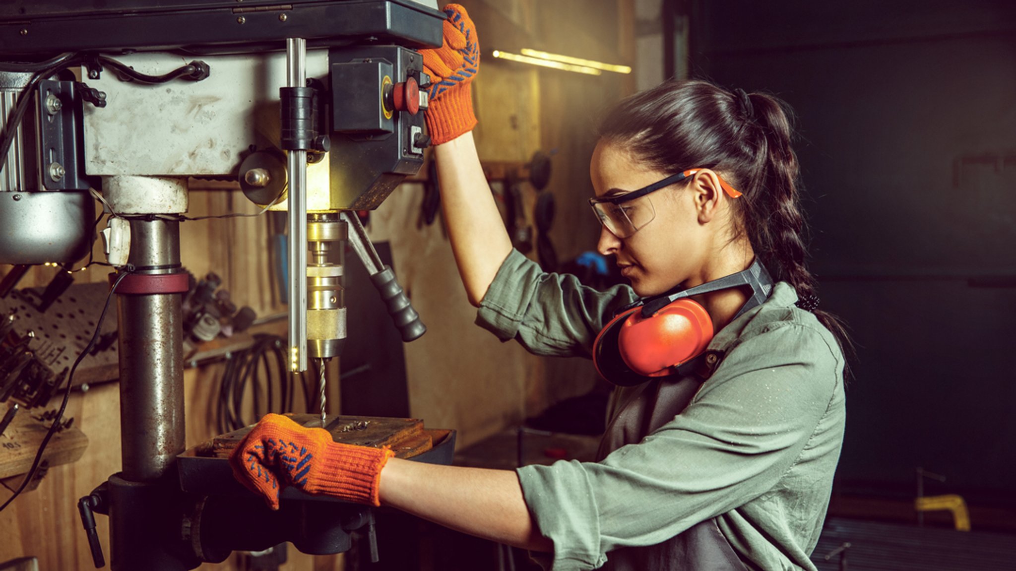 Handwerkerin arbeitet konzentriert mit einer Standbohrmaschine.