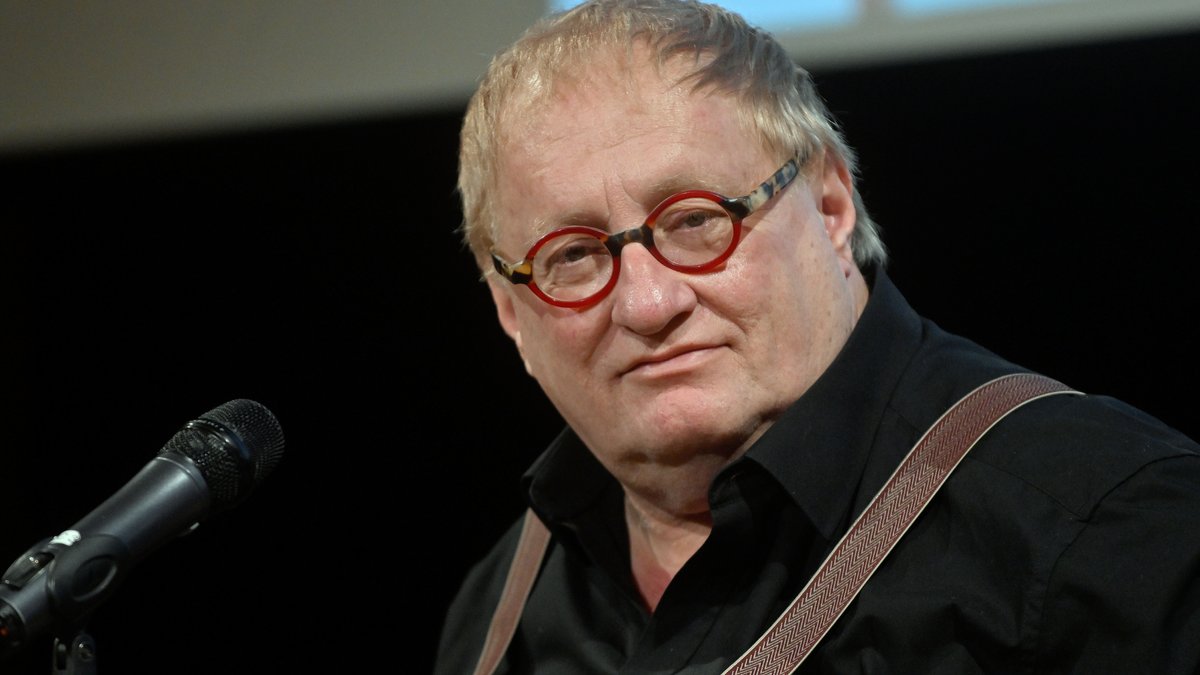 Autor Tuvia Tenenbom mit roter Brille, schwarzem Hemd und roten Hosenträgern vor einem Mikrofon
