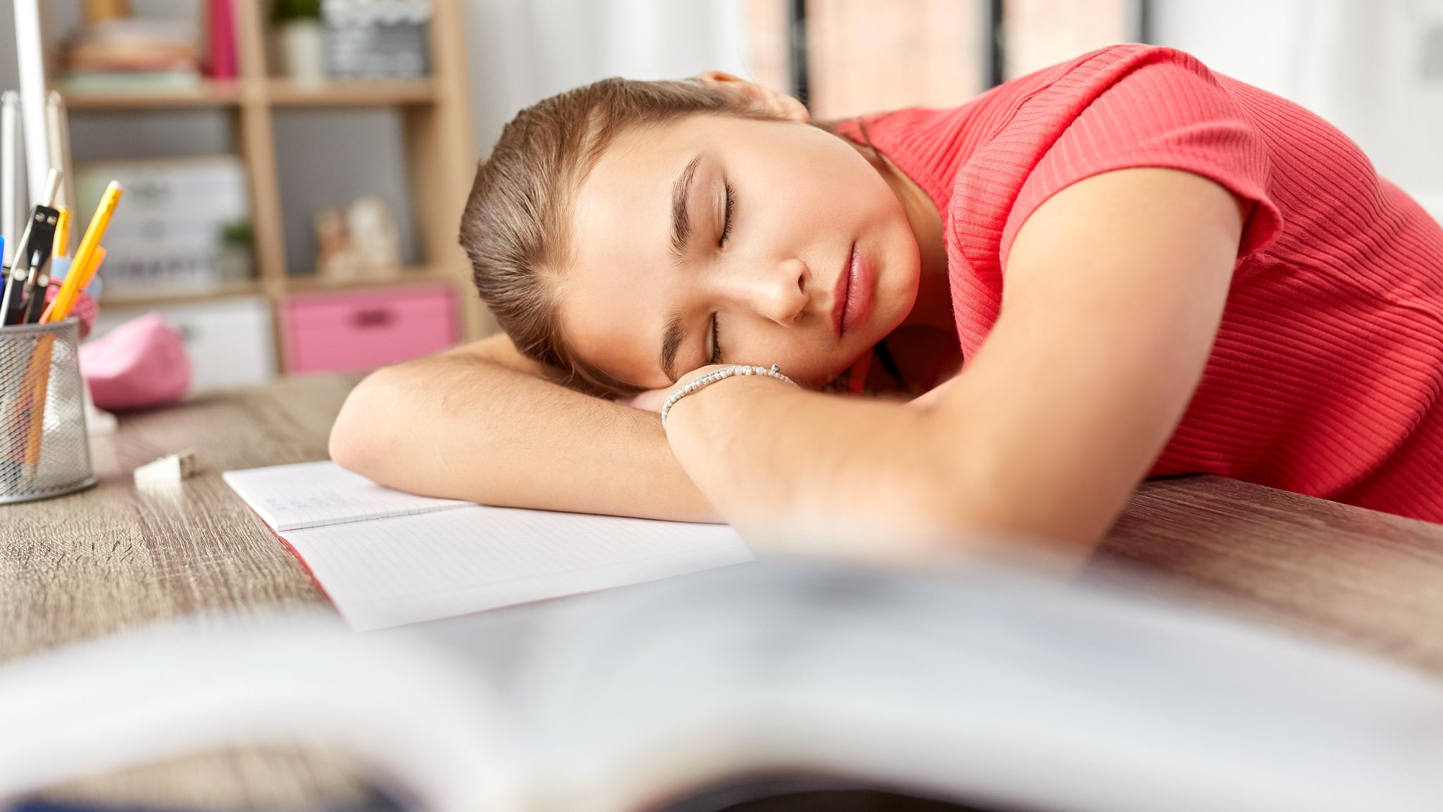 Junges Mädchen liegt mit dem Kopf müde auf dem Schreibtisch. Hat die Zeitumstellung gesundheitliche Folgen? Und warum wird überhaupt an der Uhr gedreht? | Bild: picture alliance / Zoonar | lev dolgachov Junges Mädchen liegt mit dem Kopf müde auf dem Schreibtisch. Hat die Zeitumstellung gesundheitliche Folgen? Und warum wird überhaupt an der Uhr gedreht?