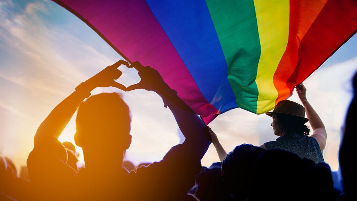 LGBT Flagge auf einer Parade mit einer Person, die ein Herz mit ihren Fingern formt.