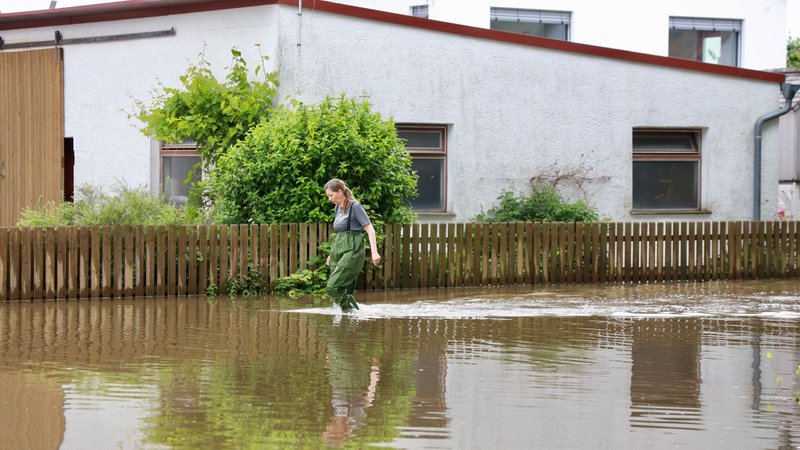 Eine Frau in wasserfesten Hosen läuft durch braunes Hochwasser, im Hintergrund ein Haus. | Bild: BR/Axel Mölkner-Kappl Eine Frau in wasserfesten Hosen läuft durch braunes Hochwasser, im Hintergrund ein Haus.