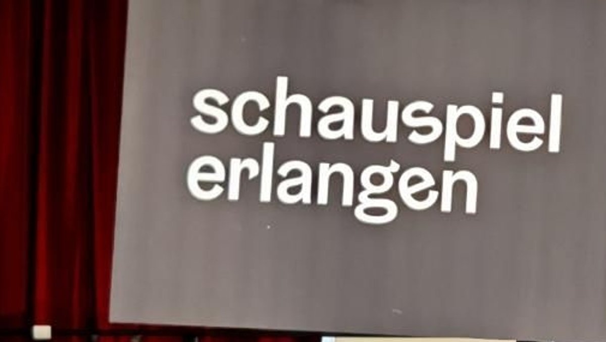 Ein Schild mit der Aufschrift "Schauspiel Erlangen" vor einem roten Theatervorhang.