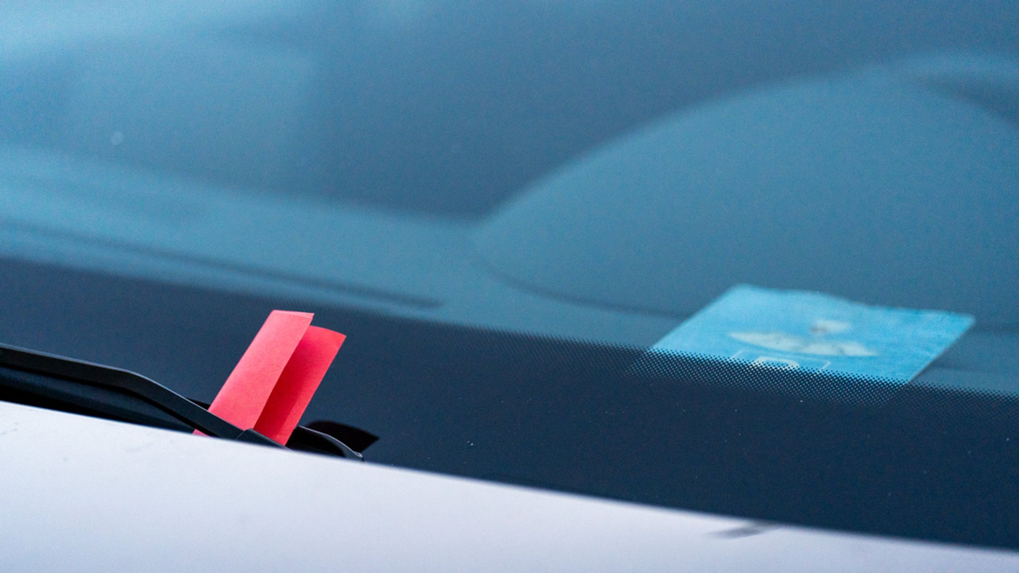 Ein roter Strafzettel klemmt an der Windschutzscheibe eines Autos. 