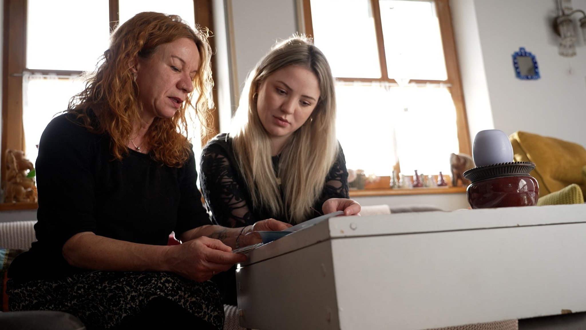 Simone E. und ihre Tochter Rebekka sitzen auf dem Sofa und schauen Familienfotos an