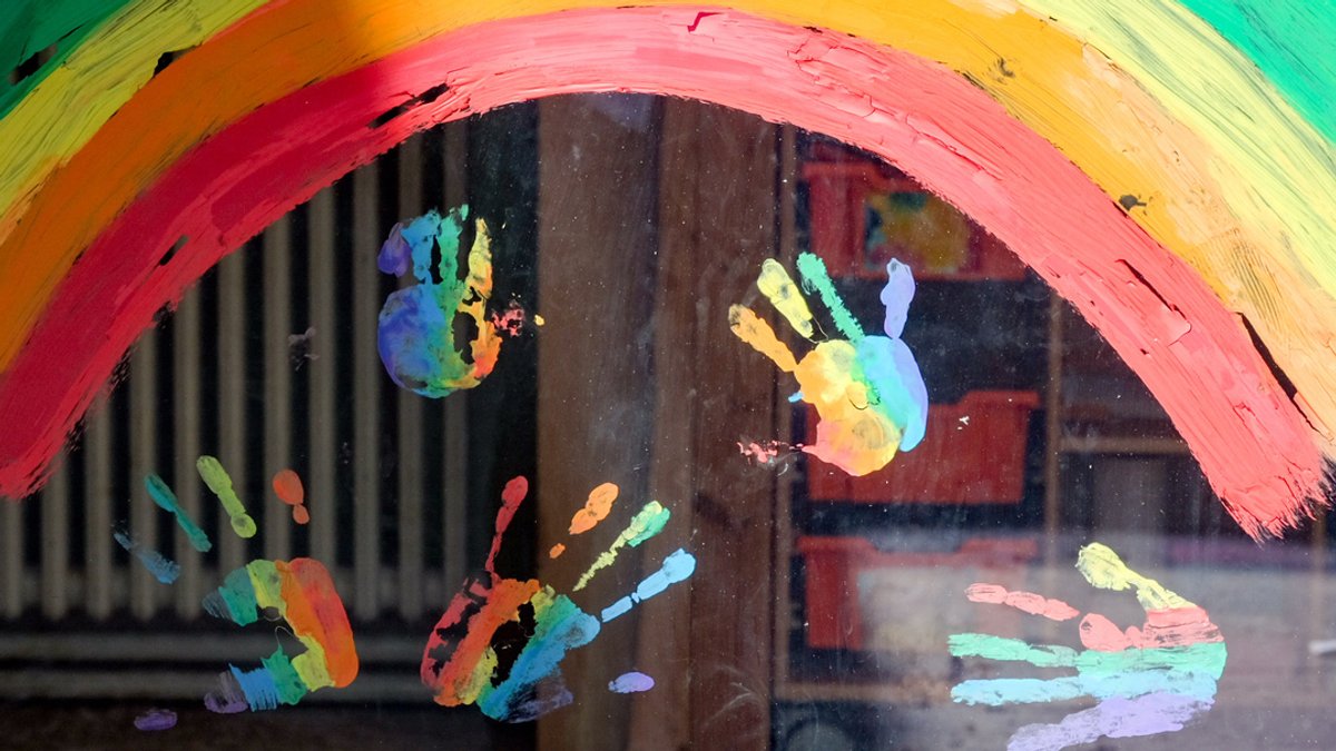 Regenbogenfarbene Handabdrücke am Fenster einer Kita.