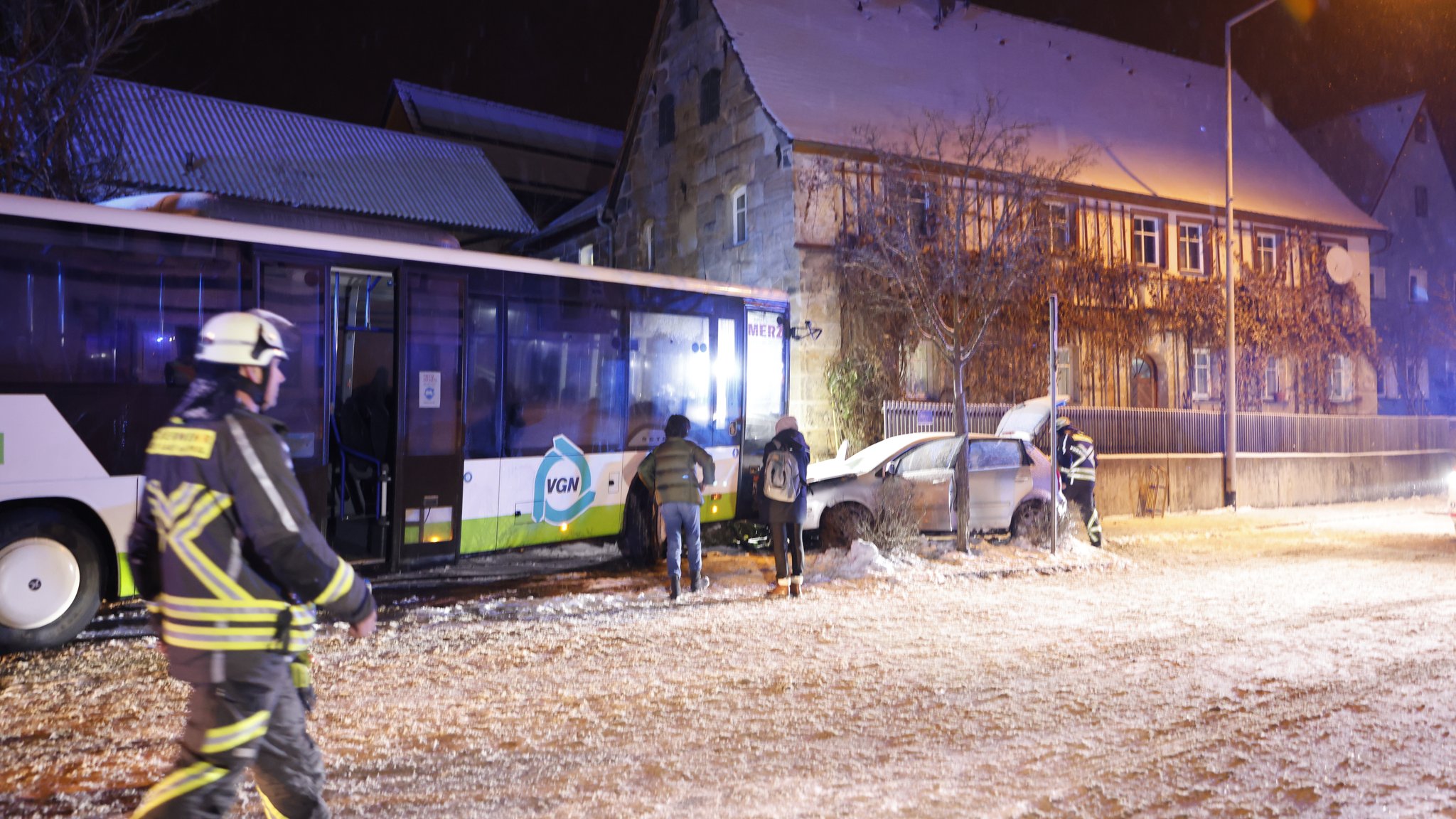 Ein Feuerwehrmann läuft bei Schneefall an einer Unfallstelle vorbei, wo ein Bus und ein Auto kollidiert sind.