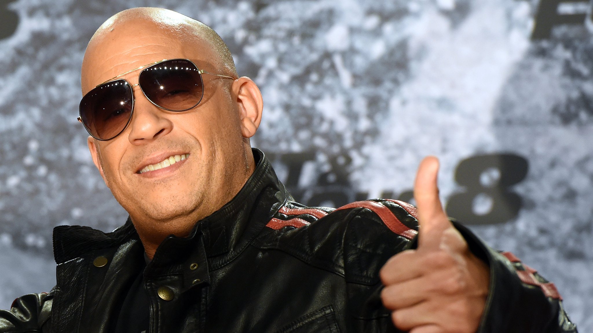 Schauspieler Vin Diesel mit Glatze, Sonnenbrille und hochgerecktem Daumen.