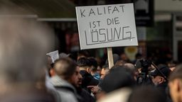 Hamburg, 27.04.24: Teilnehmer einer Islamisten-Demo halten ein Plakat mit der Aufschrift "Kalifat ist die Lösung" in die Höhe. | Bild:pa/dpa/Axel Heimken
