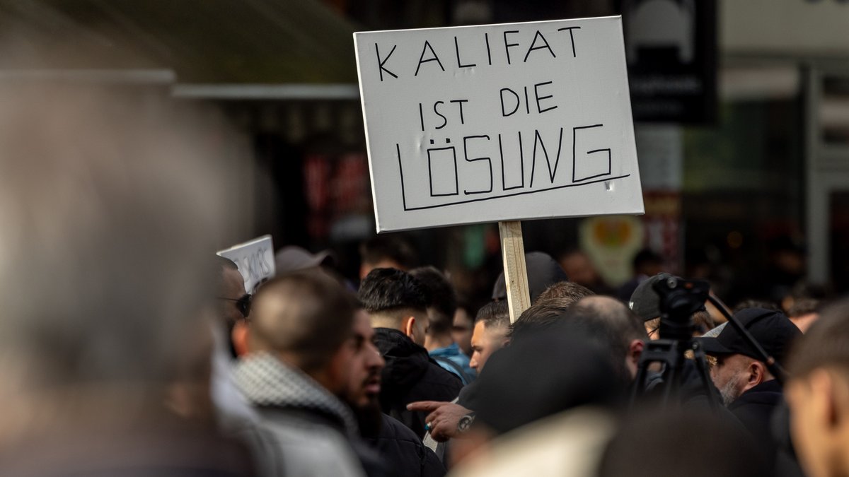 Hamburg, 27.04.24: Teilnehmer einer Islamisten-Demo halten ein Plakat mit der Aufschrift "Kalifat ist die Lösung" in die Höhe.