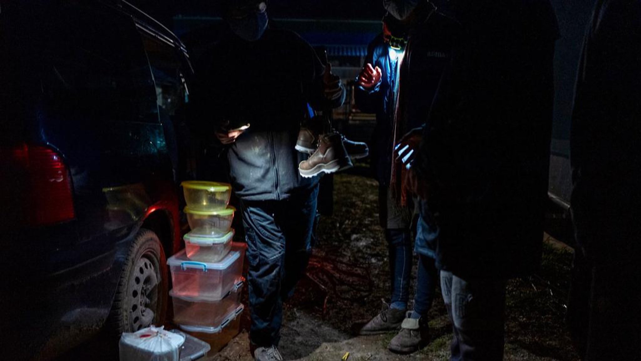 Aktivisten geben einem Mann in der Dunkelheit neben Autos ein festes Paar Winterschuhe.