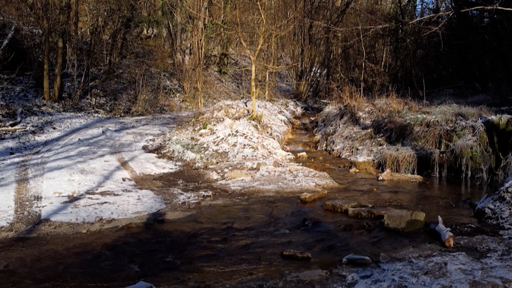 Ein Bachlauf in einem verschneiten Wald.
