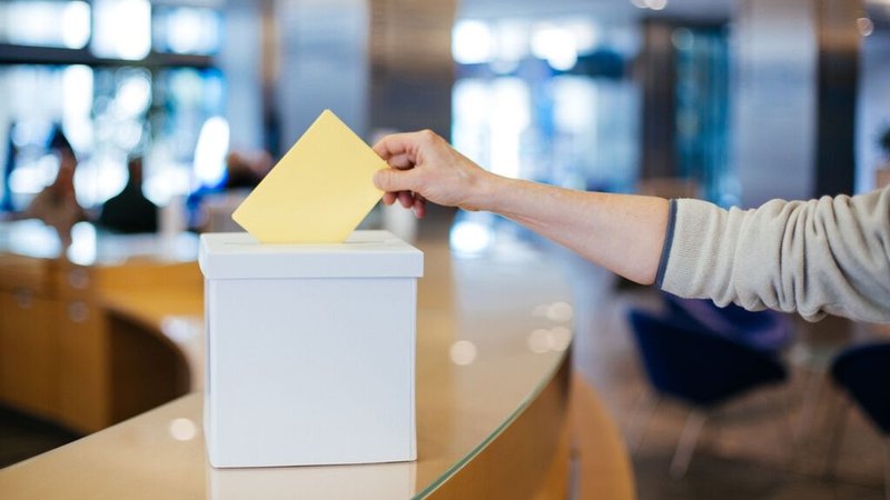 Eine Person wirft einen Wahlschein in eine Wahlurne.