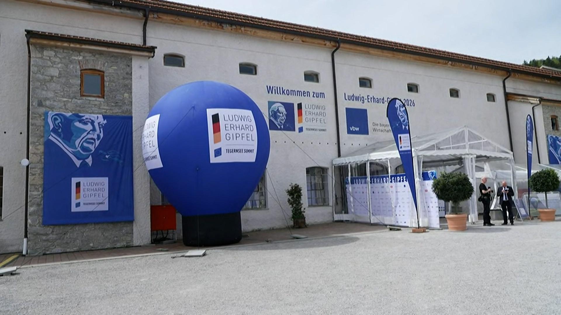 Außensicht des Veranstaltungsortes des Ludwig-Erhard-Gipfels. Vor einem hellen Gebäude stehen ein großer blauer Werbeballon mit dem Logo der Konferenz.