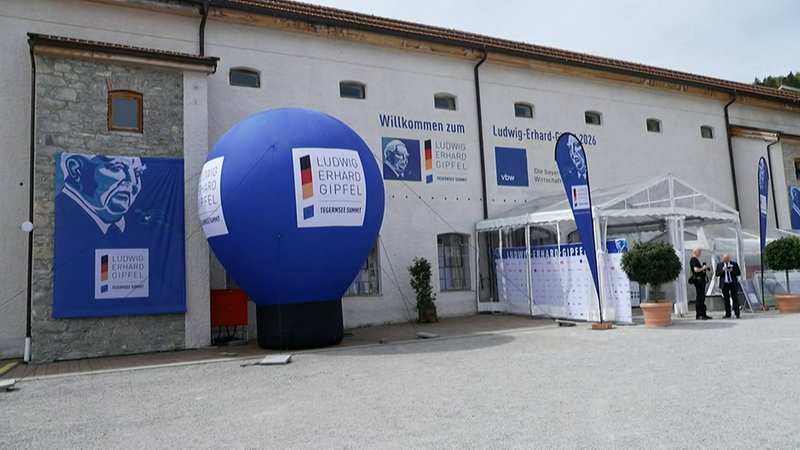 Außensicht des Veranstaltungsortes des Ludwig-Erhard-Gipfels. Vor einem hellen Gebäude stehen ein großer blauer Werbeballon mit dem Logo der Konferenz. | Bild: Bayerischer Rundfunk 2026 Außensicht des Veranstaltungsortes des Ludwig-Erhard-Gipfels. Vor einem hellen Gebäude stehen ein großer blauer Werbeballon mit dem Logo der Konferenz.