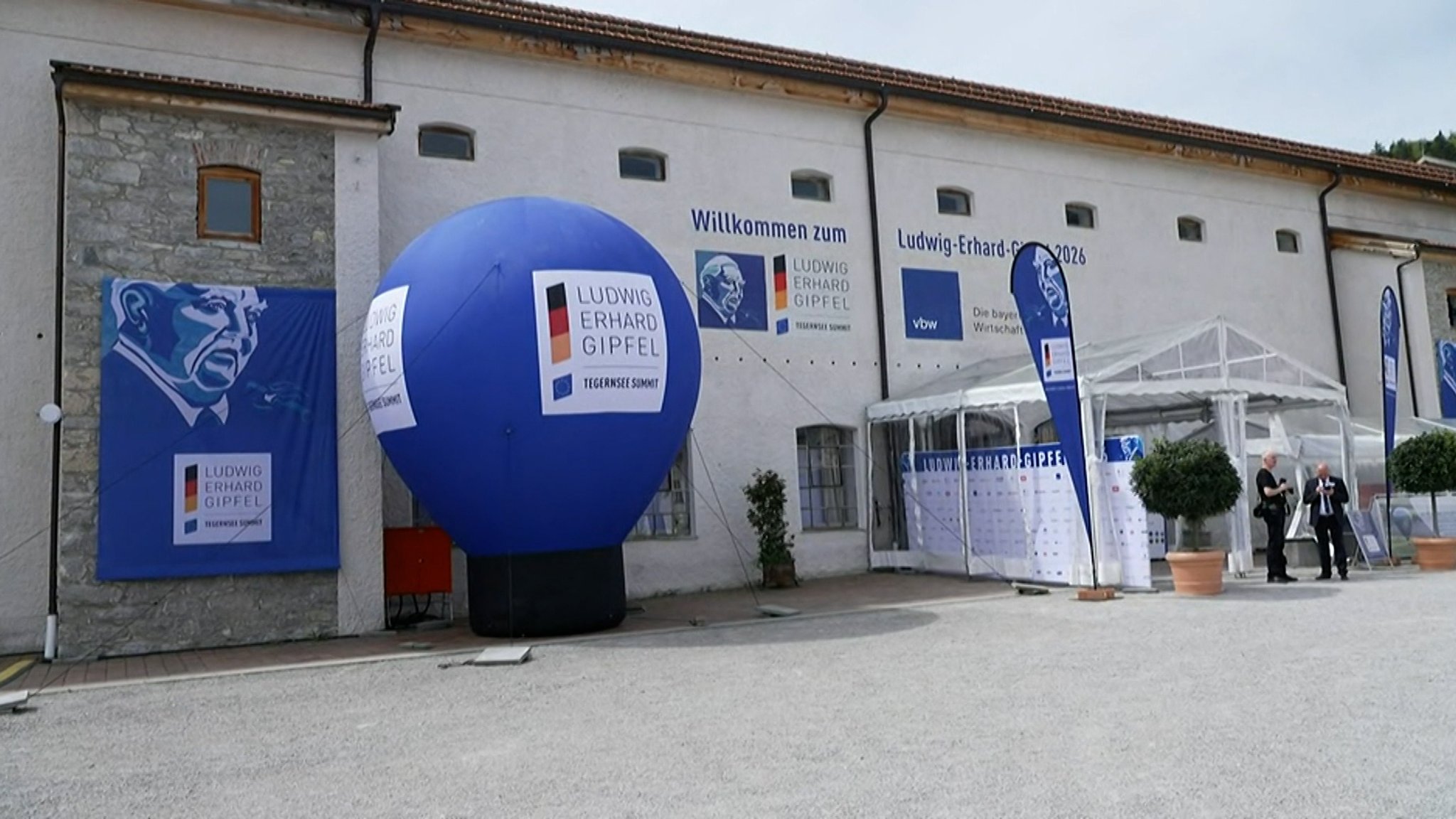 Außensicht des Veranstaltungsortes des Ludwig-Erhard-Gipfels. Vor einem hellen Gebäude stehen ein großer blauer Werbeballon mit dem Logo der Konferenz.