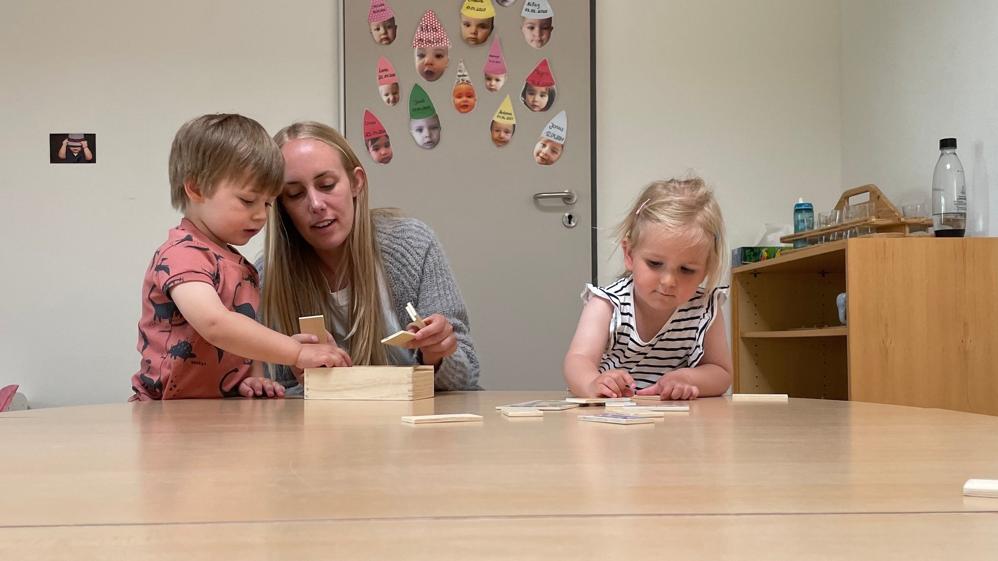 Eine Erzieherin zeigt Kindern in einer Kita wie man mit Holzteilchen spielt