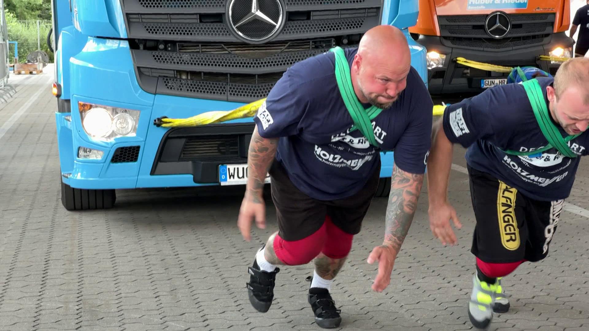 Zwei Männer ziehen mit Gurten einen Lkw