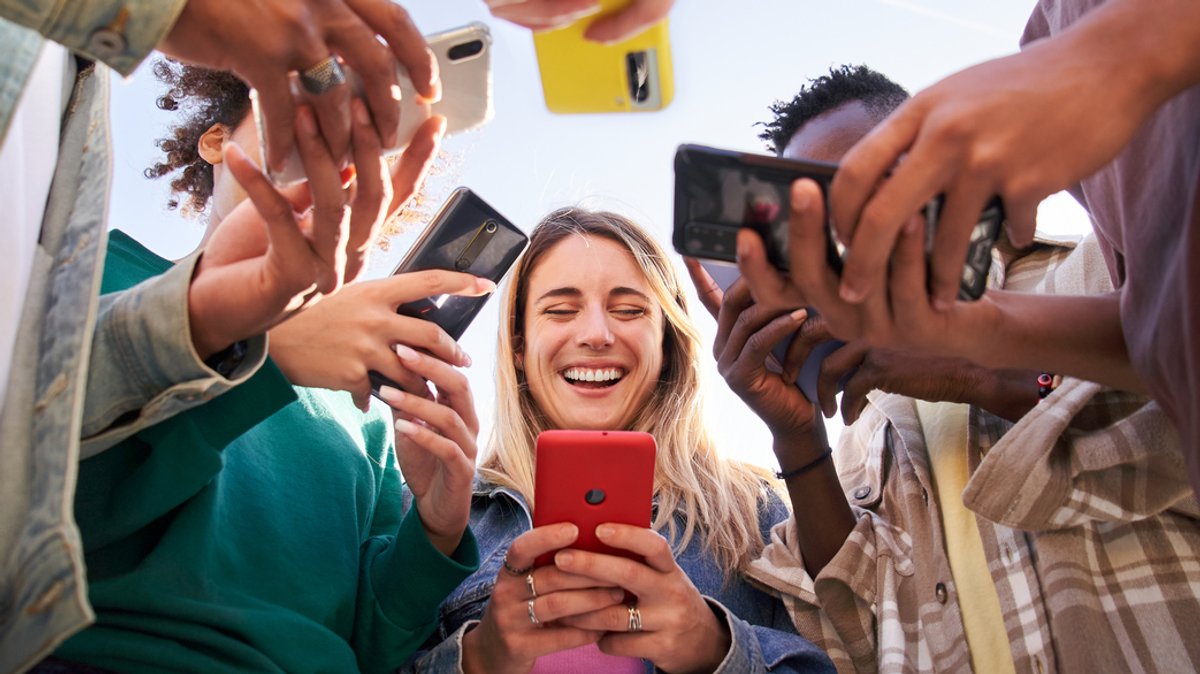 Eine Gruppe Jugendlicher steht im Kreis und alle schauen auf ihr Handy.