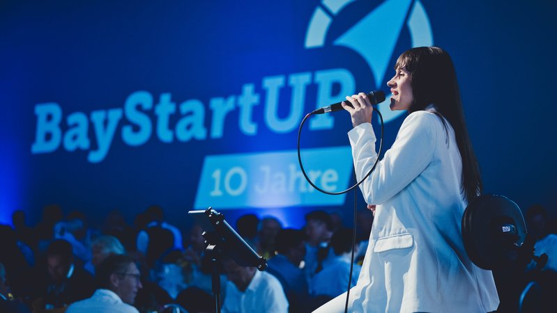 Eine junge Frau steht auf einer Bühne, im Hintergrund der Schriftzug BayStartUp | Bild: BaStartUp GmbH, Andreas Gebert Eine junge Frau steht auf einer Bühne, im Hintergrund der Schriftzug BayStartUp