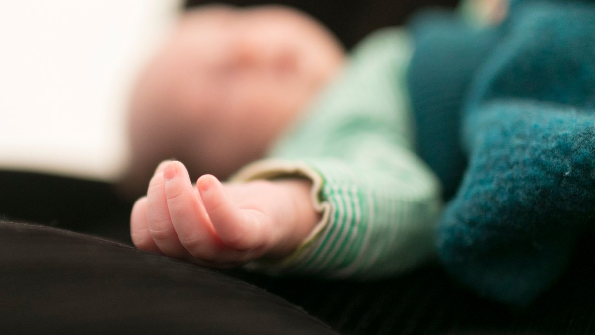 Das Bild zeigt ein schlafendes Baby mit verpixeltem Gesicht. Die ausgestreckte Hand ist im Fokus.