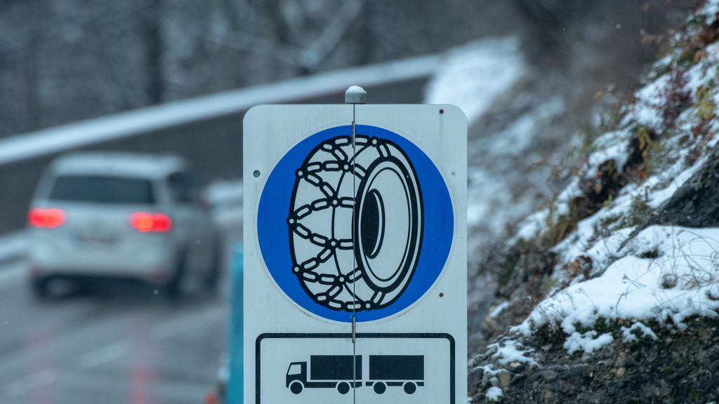 Schild an einer verschneiten Straße, dass auf Schneeketten hinweist.
