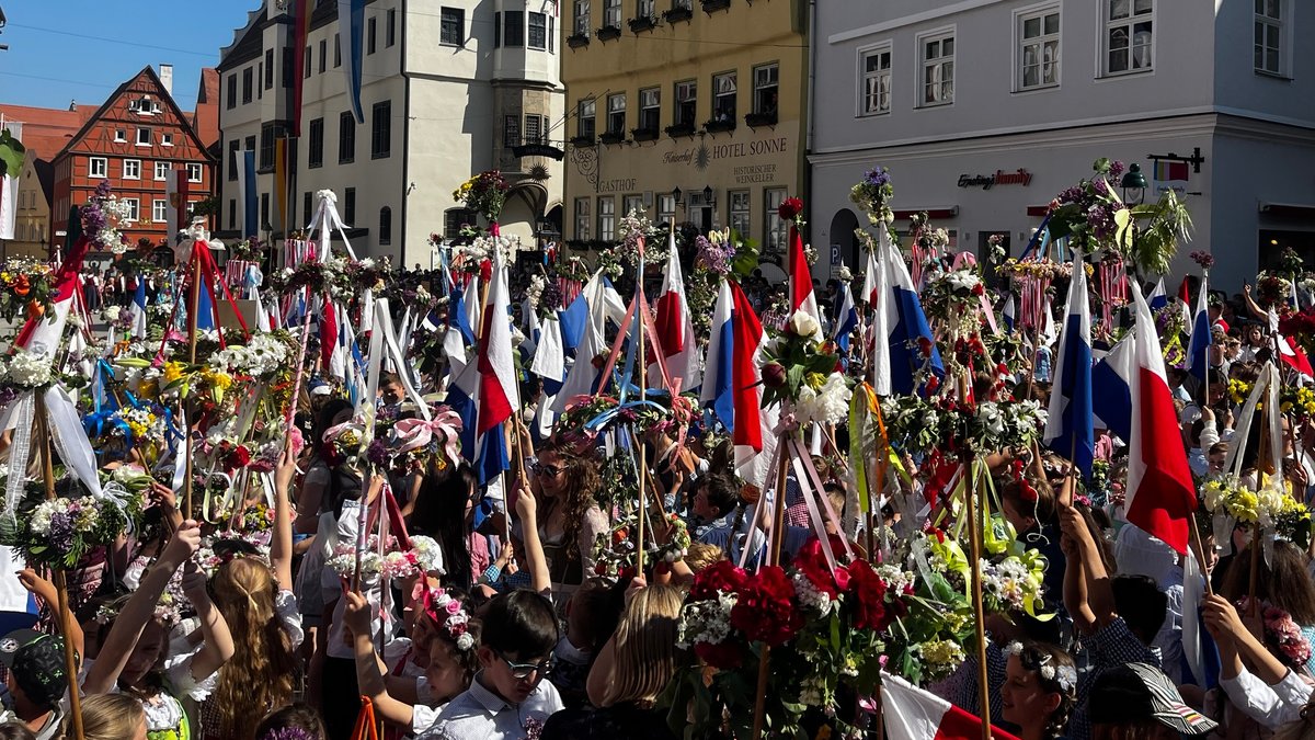 Kinder halten beim Stabenfest in Nördlingen mit Blumen und Fahnen geschmückte Holzstäbe in die Luft.