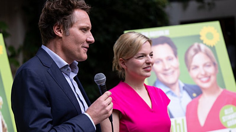 Ludwig Hartmann und Katharina Schulze stehen vor Wahlplakaten der Grünen.
