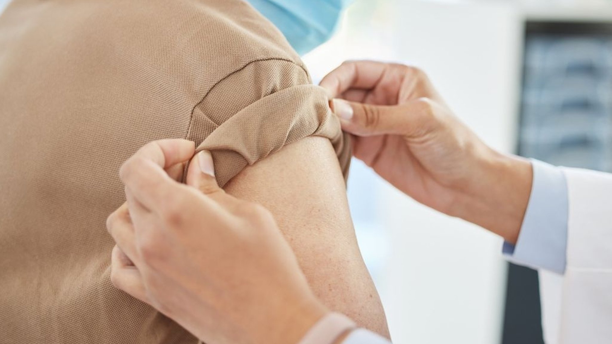 Die Hände einer Ärztin krempeln den Ärmel eines Patienten hoch.