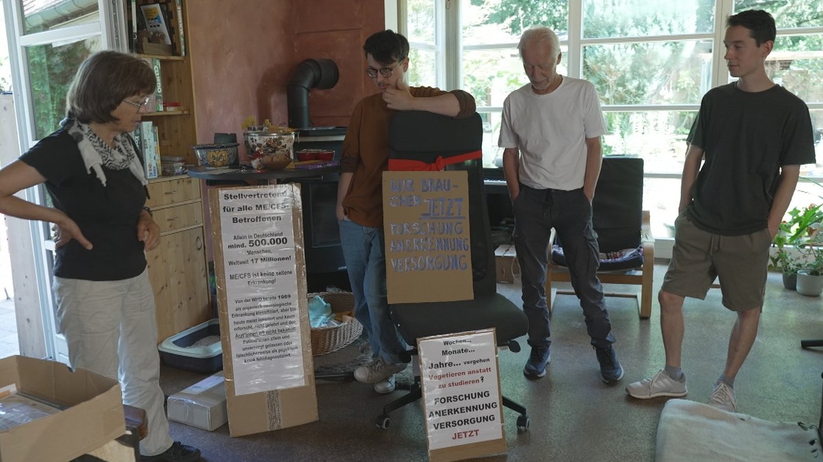 Familie Masin aus München vor der Demonstration: Vier Personen stehen mit Plakaten in einem Wohnzimmer.