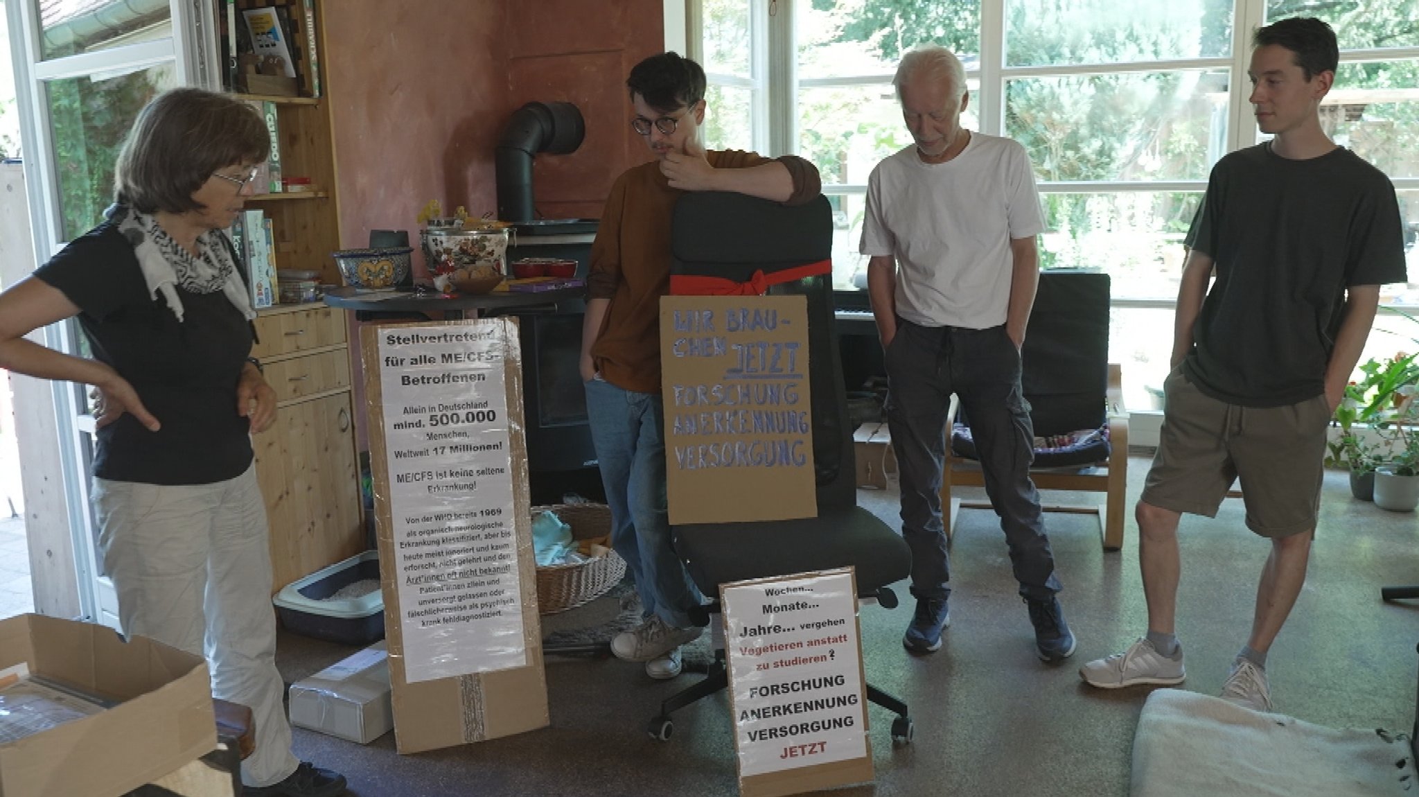 Familie Masin aus München vor der Demonstration: Vier Personen stehen mit Plakaten in einem Wohnzimmer.