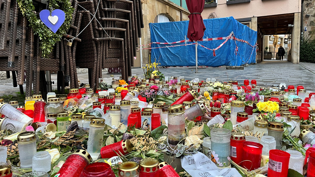 Kerzen und Blumen stehen auf dem Boden einer Straße. 