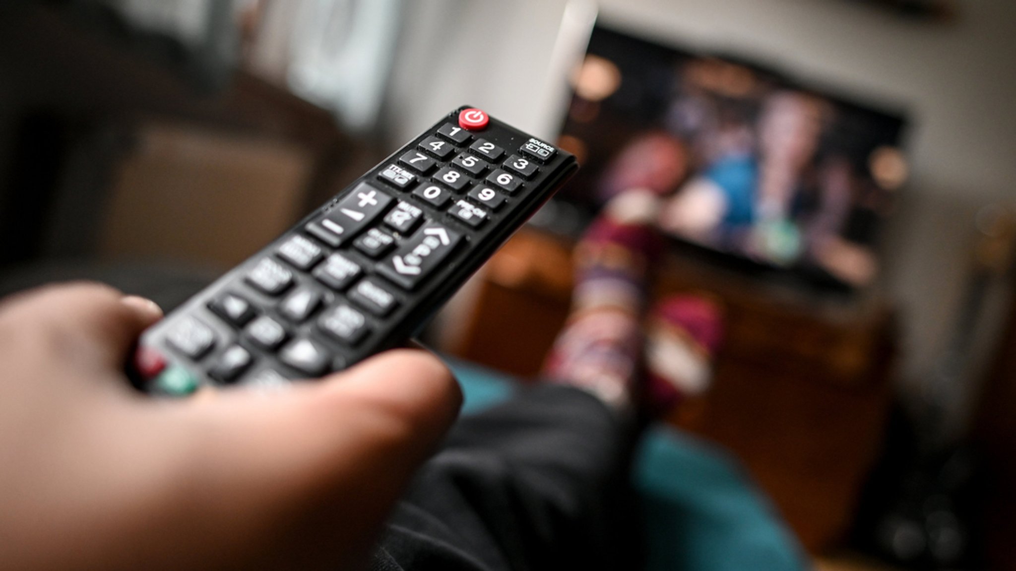 Ein junger Mann sitzt mit einer Fernbedienung vor dem Fernseher.