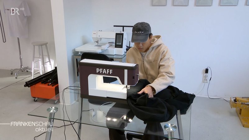 Ein junger Mann sitzt an einer Nähmaschine und näht. | Bild: BR-Studio Franken Ein junger Mann sitzt an einer Nähmaschine und näht.
