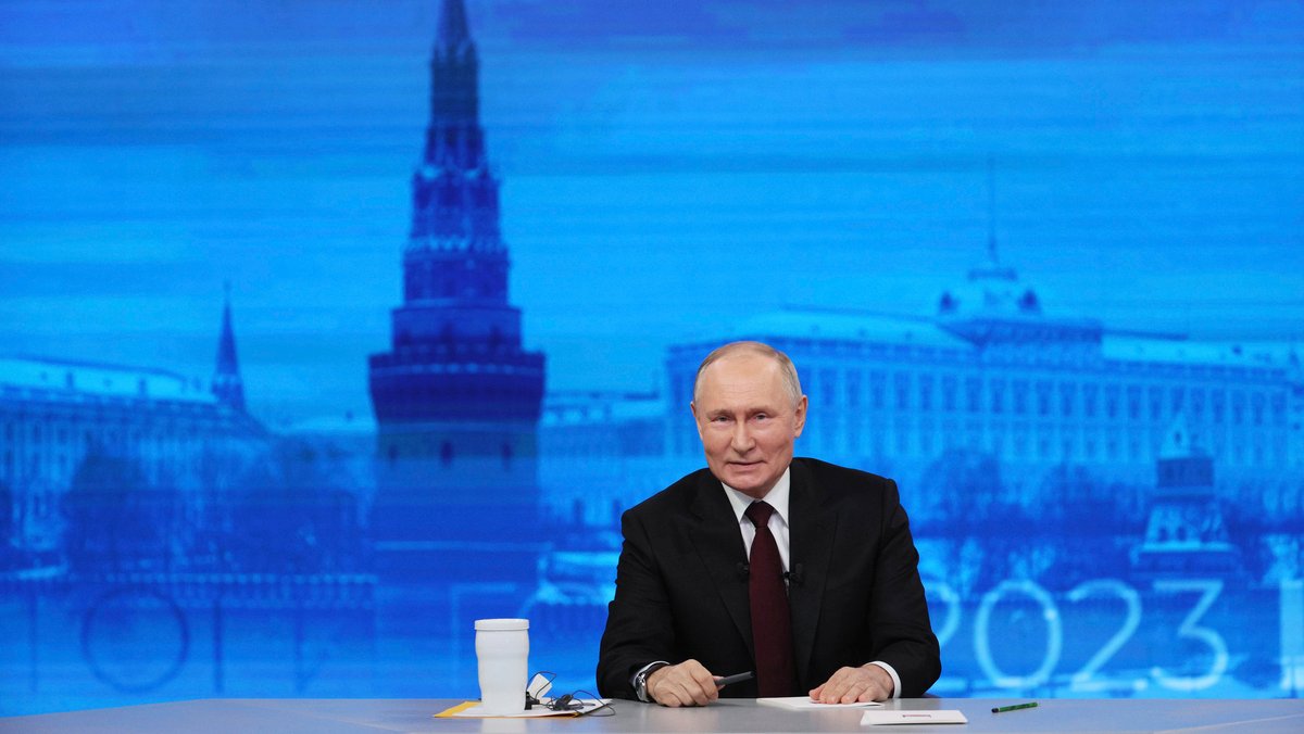 Man sieht Wladimir Putin, Präsident von Russland, während seiner jährlichen Pressekonferenz an einem Tisch sitzen, im Hintergrund der Rote Platz..