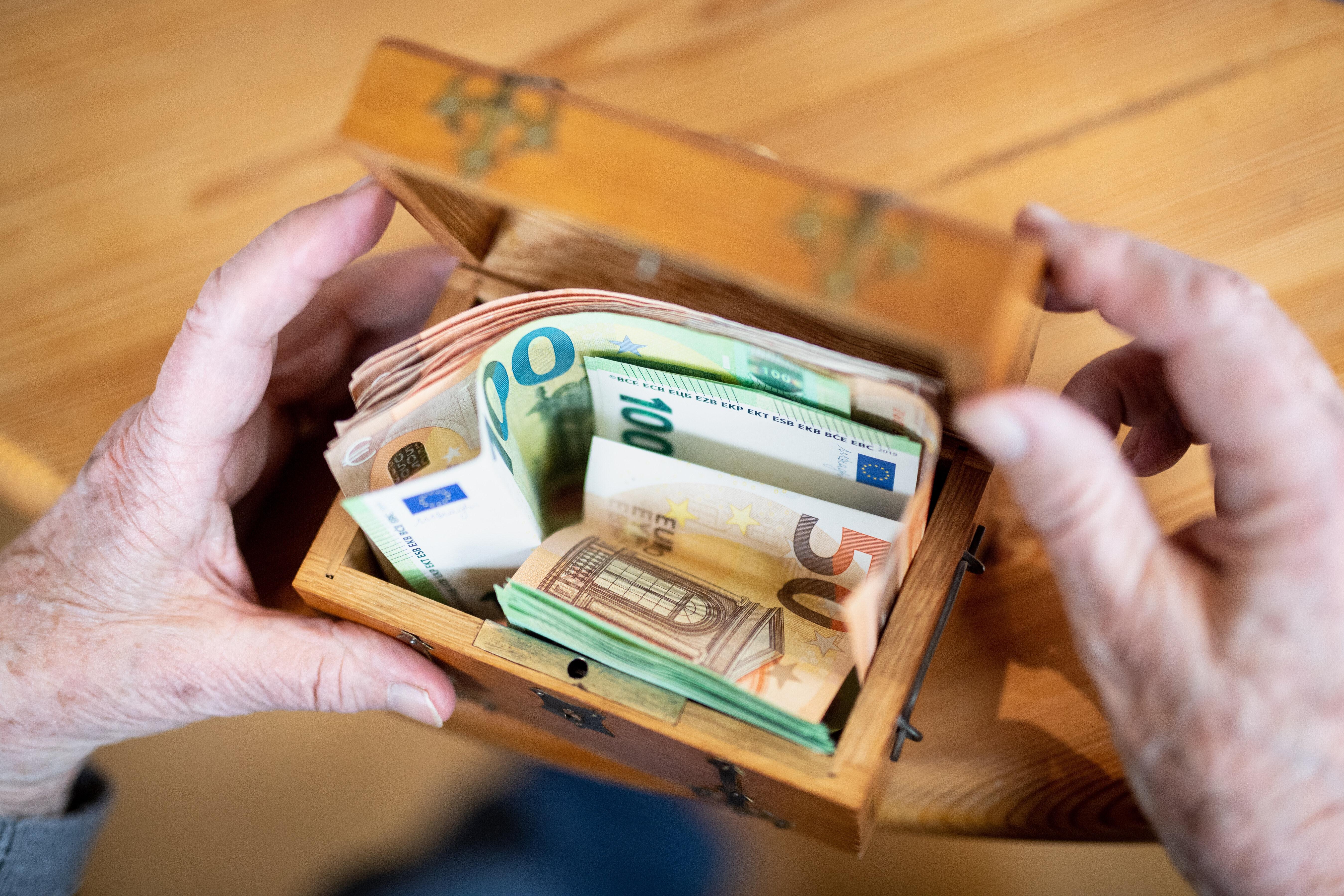 Symbolbild: Jemand zählt mehrere hundert Euro in Geldscheinen in einer kleinen Schatztruhe ab.
